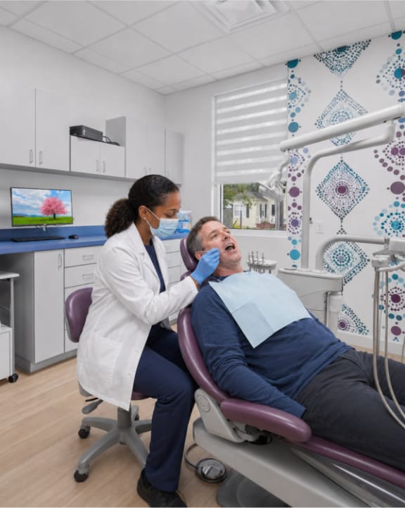 A dentist performing an oral cancer screening of a patient’s mouth and neck