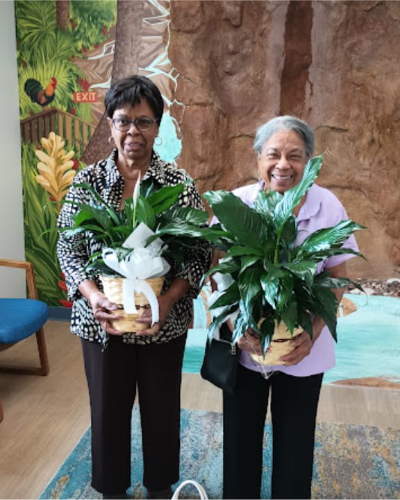 Two women holding potted plants in the office lobby